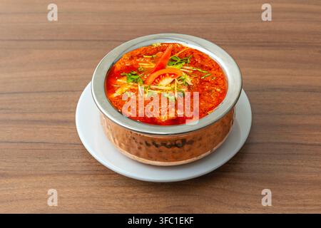 Curry au agneau Rogan Josh dans un bol en cuivre, garni de coriandre, de lamelles de gingembre et de rondelles de tomates fraîches. Banque D'Images