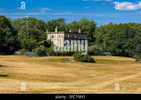 Ruines de la maison Piercefield du XVIIIe siècle à Chepstow, au Pays de Galles, façade en pierre néoclassique abandonnée encadrée par une forêt dense et verte derrière une parcelle séchée par le soleil Banque D'Images