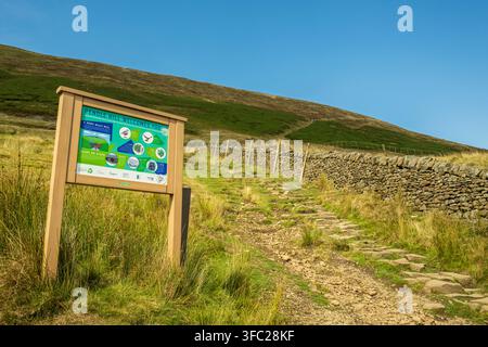 Un panneau d'information "Pendle Hill vous souhaite la bienvenue" se trouve au début d'un sentier pavé de pierres menant aux pentes herbeuses de Pendle Hill dans le Lancashire Banque D'Images