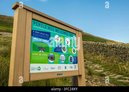 Un panneau d'information "Pendle Hill vous souhaite la bienvenue" se trouve au début d'un sentier pavé de pierres menant aux pentes herbeuses de Pendle Hill dans le Lancashire Banque D'Images