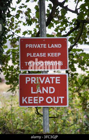 Panneaux d'avertissement rouges empilés sur un poteau métallique indiquant Terrain Privé Veuillez Rester sur les Sentiers et Terrain Privé Défense d'Entrée. Banque D'Images