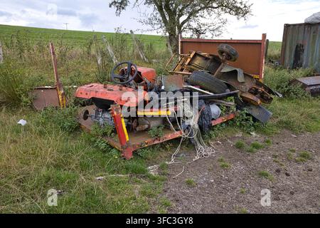 tas de ferraille de ferme abandonnée, pièces de tondeuse à gazon cassées, pneus et ferraille métallique déposés sur une remorque près du bord d'un champ. Banque D'Images