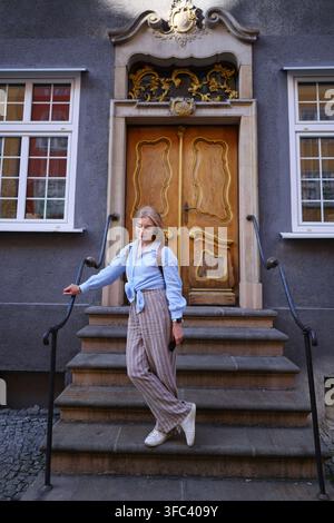 Femme en visite touristique dans une ville historique européenne, posant devant une porte ornée et une façade architecturale traditionnelle. Banque D'Images