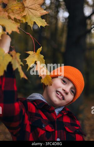 Garçon heureux jouant avec des feuilles d'automne jaunes dans le parc Banque D'Images