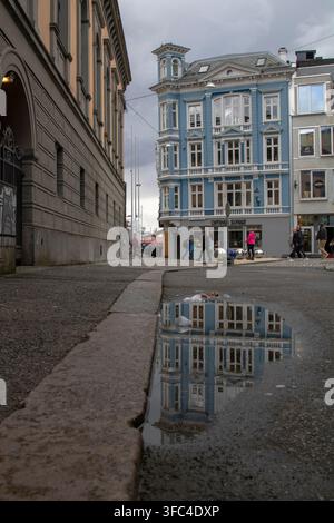 Architecture bleue se reflétant dans une flaque de rue par une journée nuageuse à Bergen, Norvège Banque D'Images