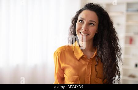 Jeune femme souriante du Moyen-Orient portant une chemise orange dans un bureau lumineux, concept d'affaires Banque D'Images