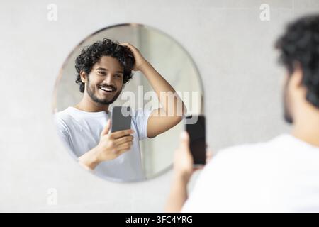 Jeune homme sud-asiatique souriant prenant un selfie devant le miroir, cadre de salle de bain Banque D'Images