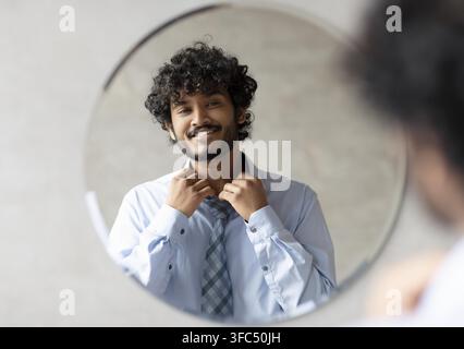 Jeune homme ajustant sa cravate devant le miroir, souriant, concept d'affaires Banque D'Images