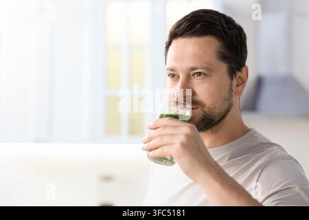 Homme buvant un smoothie vert dans un verre à l'intérieur, espace pour du texte Banque D'Images