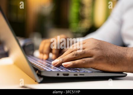 Gros plan d'un homme d'affaires noir faisant une réflexion critique et relisant des documents avant de transcrire des données sur un cahier, debout dans le bureau la nuit. Documenter des idées importantes. Banque D'Images