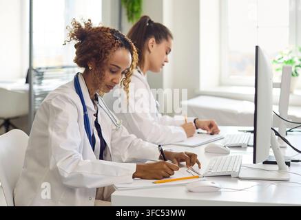 Médecines féminines analysant les données des patients et prenant des notes sur des ordinateurs dans la clinique Banque D'Images