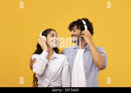 Couple sud-asiatique heureux écoutant de la musique ensemble avec des écouteurs, souriant, fond jaune Banque D'Images