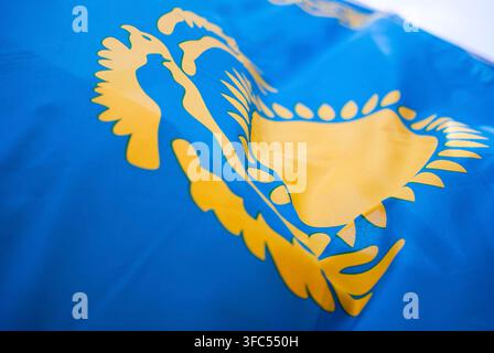 Un macro plan détaillé centré sur l'aigle des steppes stylisé jaune et les ornements solaires de la drapeau national bleu ciel du Kazakhstan flottant au vent. Banque D'Images