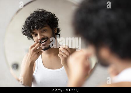 Jeune homme utilisant la soie dentaire devant le miroir de la salle de bain, se concentrant sur les soins dentaires Banque D'Images