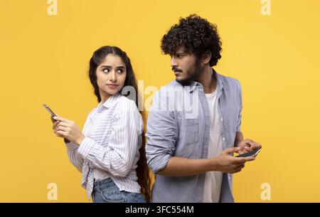 Jeune femme et homme sud-asiatiques utilisant des smartphones, se faisant face tout en se tenant dos à dos Banque D'Images