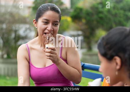 Close up d'une mère latine mangeant une glace tout en regardant ses filles au parc Banque D'Images