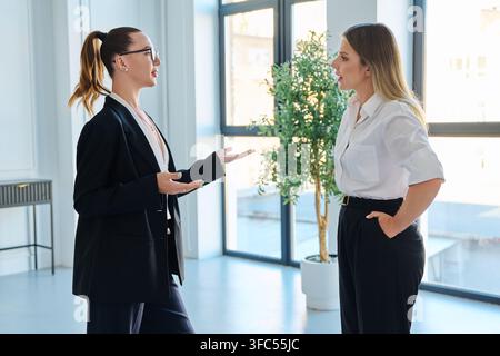 Deux femmes d'affaires debout et discutant lors d'une réunion dans un bureau moderne et lumineux Banque D'Images