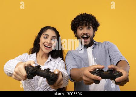 Jeun couple heureux jouant à des jeux vidéo ensemble avec des manettes, fond jaune Banque D'Images