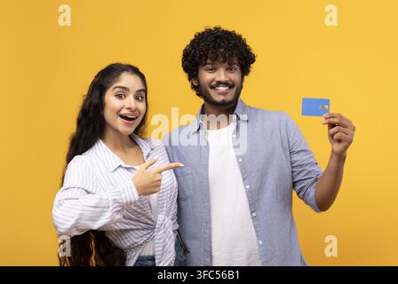 Couple sud-asiatique heureux souriant et tenant une carte de crédit, concept commercial, fond jaune Banque D'Images