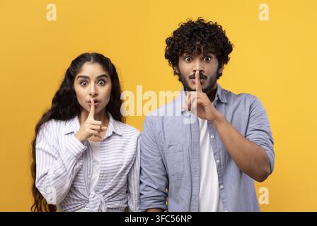 Jeune homme et femme sud-asiatiques faisant un geste de silence, isolés sur fond jaune Banque D'Images