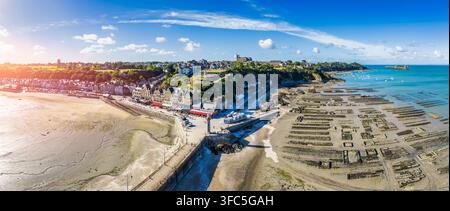 Vue aérienne de la ville côtière de Cancale avec son port historique, ses bâtiments traditionnels en pierre et ses vastes parcs à huîtres exposés à marée basse, Franc Banque D'Images