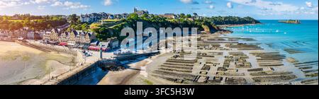 Vue aérienne de la ville côtière de Cancale avec son port historique, ses bâtiments en pierre et ses vastes parcs à huîtres exposés à marée basse en France. Banque D'Images