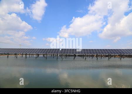 Sous un ciel bleu clair parsemé de nuages blancs, des rangées de panneaux photovoltaïques solaires sont soigneusement installées sur l'eau, formant un réseau spectaculaire. Leur réflexion Banque D'Images