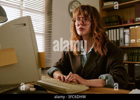 Femme concentrée tapant sur un ordinateur rétro dans un bureau vintage Banque D'Images