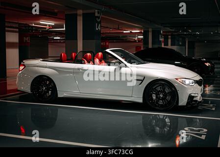 Profil latéral d'une BMW M4 décapotable blanche avec le toit baissé et l'intérieur en cuir rouge à l'intérieur d'un garage souterrain. Banque D'Images