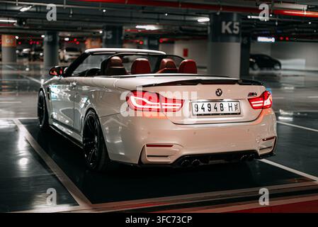 Vue arrière trois quarts d'une BMW M4 décapotable blanche avec le toit baissé, des sièges rouges et des feux arrière allumés dans un garage. Banque D'Images