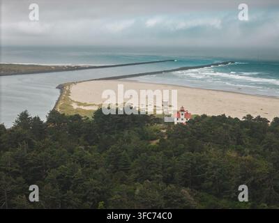 Vue aérienne du phare de Yaquina Bay entouré d'une forêt dense, d'une plage de sable et de jetées rocheuses s'étendant dans l'océan Pacifique à Newport, Oregon Banque D'Images
