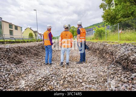 Trois ouvriers du bâtiment portant des gilets de sécurité et des casques se tiennent sur une surface de gravier, conversion de la station électrification Leonhard Weiss, Waldshut. ge Banque D'Images