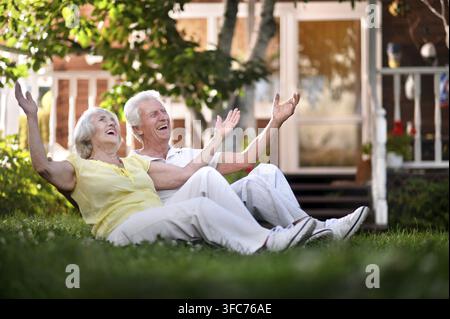 Un charmant couple de personnes âgées est assis sur l'herbe près de leur maison Banque D'Images
