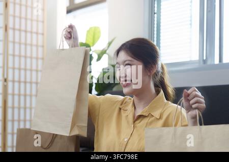 Une jeune femme enthousiaste tient des sacs de courses et célèbre ses achats en ligne réussis dans un environnement domestique confortable Banque D'Images