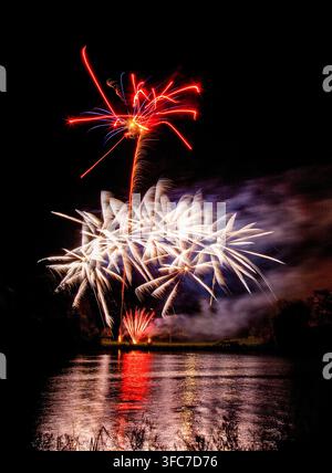 Affichage de feux d'artifice colorés et vifs éclatant au-dessus d'un lac avec des reflets dramatiques rouges et blancs dans l'eau Banque D'Images