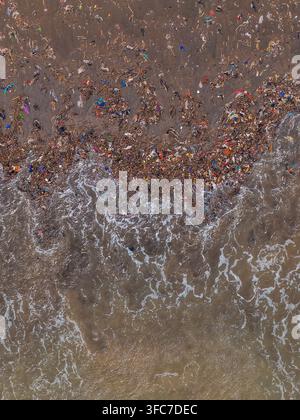 Vue aérienne de la pollution plastique et des débris éparpillés le long du rivage sablonneux avec les vagues de l'océan qui déferlent sur la plage en Indonésie. Banque D'Images