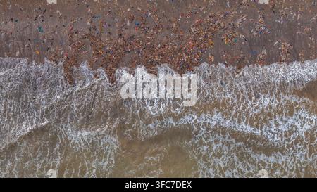 Vue aérienne d'une plage fortement polluée par des déchets plastiques et des débris, avec des vagues de l'océan qui déferlent sur le rivage sablonneux en Indonésie. Banque D'Images