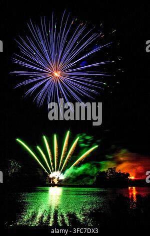 Spectacle de feux d'artifice éclatants et colorés éclatant au-dessus d'un lac avec des reflets dramatiques verts et orange dans l'eau Banque D'Images