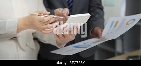 Deux personnes d'affaires travaillent ensemble pour analyser des données financières sur une tablette et des documents, en mettant l'accent sur le travail d'équipe dans un environnement d'entreprise Banque D'Images