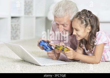 Grand-père émotionnel et petite-fille jouant à un jeu d'ordinateur avec ordinateur portable à la maison Banque D'Images