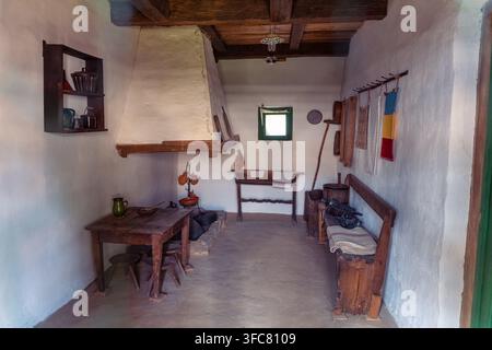 Intérieur rustique d'une vieille maison roumaine avec meubles en bois, cheminée et objets ménagers traditionnels Banque D'Images