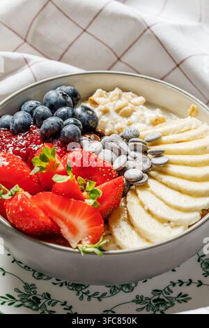 Bol de flocons d'avoine pour un petit-déjeuner sain garni de myrtilles fraîches, de fraises tranchées, de pépites de chocolat et de banane Banque D'Images