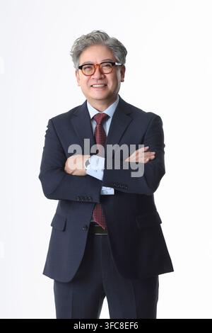 Homme d'affaires et cadre coréen âgé et confiant souriant, les bras croisés, devant un fond blanc. Banque D'Images