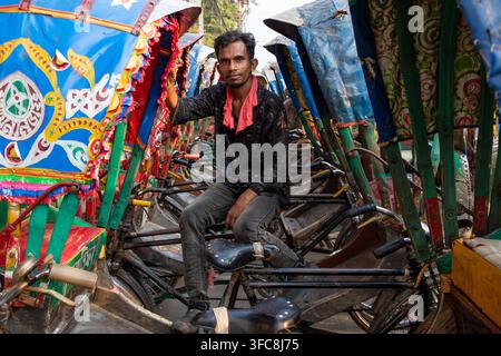 Dhaka, Bangladesh - 17 mai 2024 : Vue d'un tireur de rickshaw assis sur sa rickshaw cyclique traditionnelle et colorée dans les rues animées. Banque D'Images