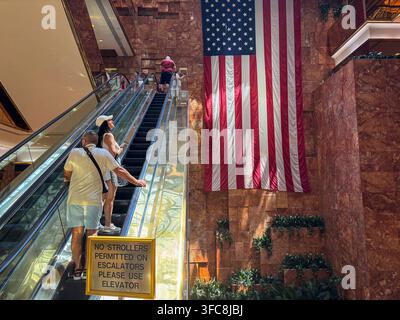 Les visiteurs empruntent les escalators de l'atrium du Trump Tower à côté d'un drapeau américain accroché au mur de marbre rose. New York, New York, États-Unis, 7 Augu Banque D'Images