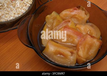 Tranches de pommes cuites ou cuites au four dans un bol en verre sombre. Vue rapprochée à angle élevé d’un composant de petit-déjeuner sain avec porridge de flocons d’avoine et muesli o Banque D'Images