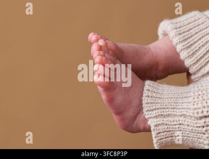 Pieds de nouveau-né douillets avec pantalon tricoté détail en gros plan sur fond neutre chaud Banque D'Images