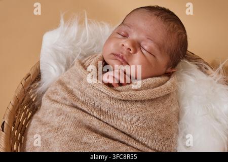 Bébé nouveau-né endormi enveloppé dans une couverture douillette allongé dans un panier en osier Portrait de nouveau-né Banque D'Images