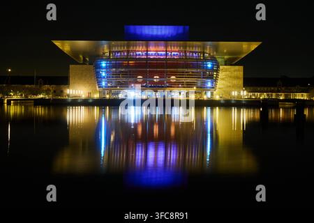 L’Opéra Royal du Danemark à Copenhague la nuit, avec les lumières bleues du toit se reflétant dans les eaux du port lors d’une pose longue. Banque D'Images