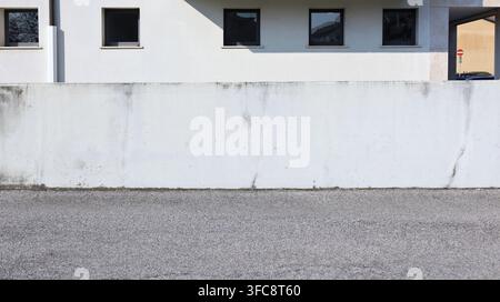 Clôture en plâtre blanc au bord de la route avec façade de bâtiment blanc et rangée de fenêtres en arrière-plan. Porche sur le bord droit, rue devant. Fond pour texte Banque D'Images